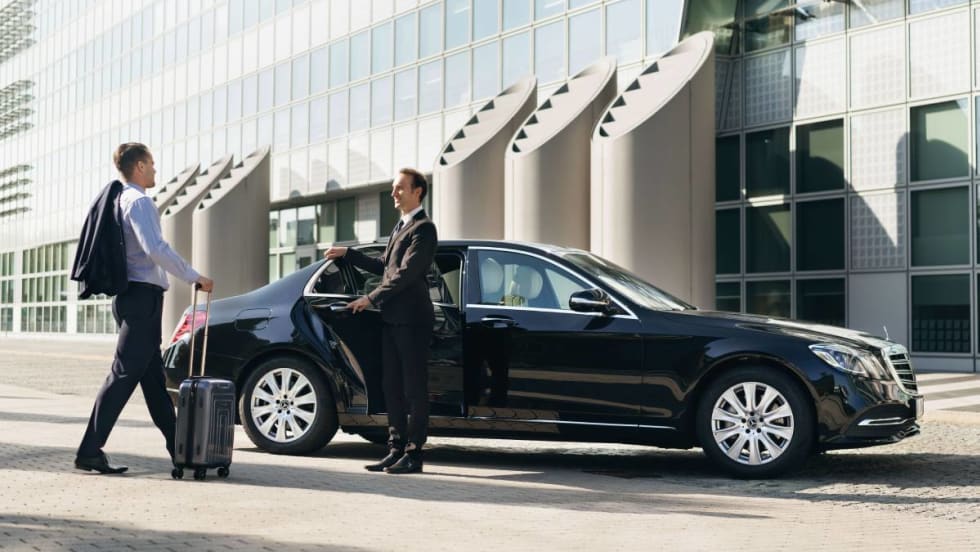 Chauffeured client being greeted by chauffeur steps into the back of a luxury black Mercedes-Benz operated by Blacklane.