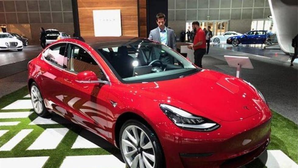 A bright shiny red Tesla 3 EV in a showroom.