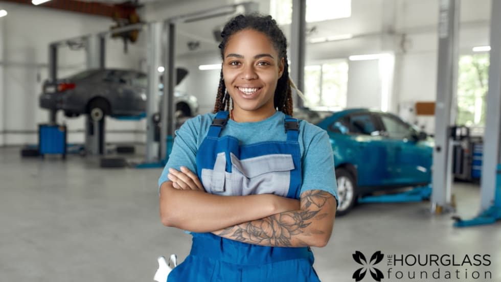 A woman in a blue shirt and apron stands in an automotive suite with her arms crossed. 