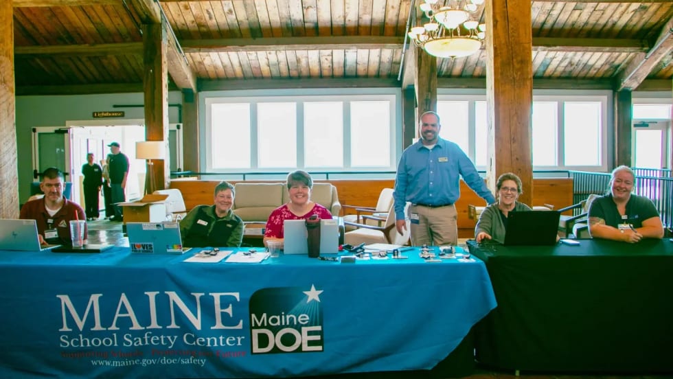 Conference registration table staffed by Maine School Safety Center team members assisting attendees with check-in at a school safety and transportation event.