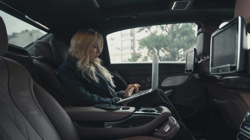 Businesswoman working on a laptop while riding in the backseat of a chauffeured car.