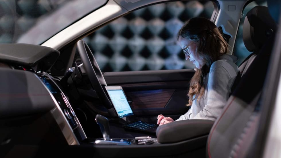 Data analyst looking at computer screen while seated in front of vehicle.