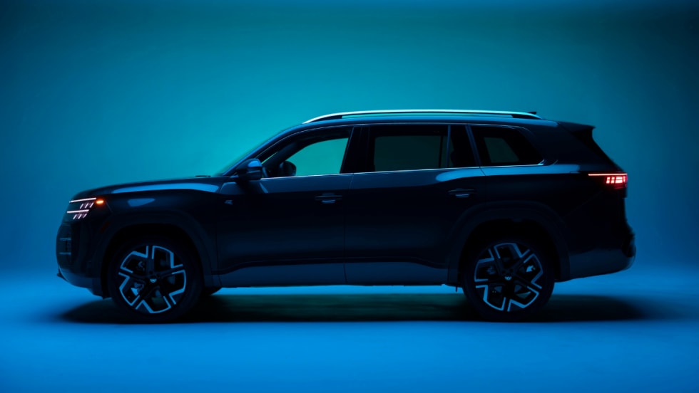 Side profile of a dark Volkswagen Atlas SUV in a studio setting with blue lighting, highlighting updated design and exterior styling.