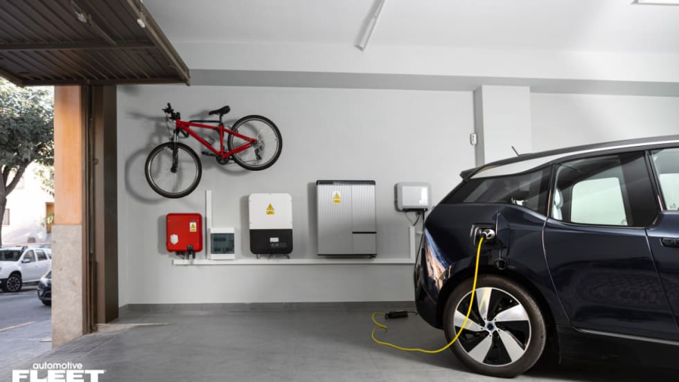 Electric vehicle charging in a home garage with wall-mounted charging and energy systems, illustrating WEX EV At-Home fraud protection and fleet charging verification technology.