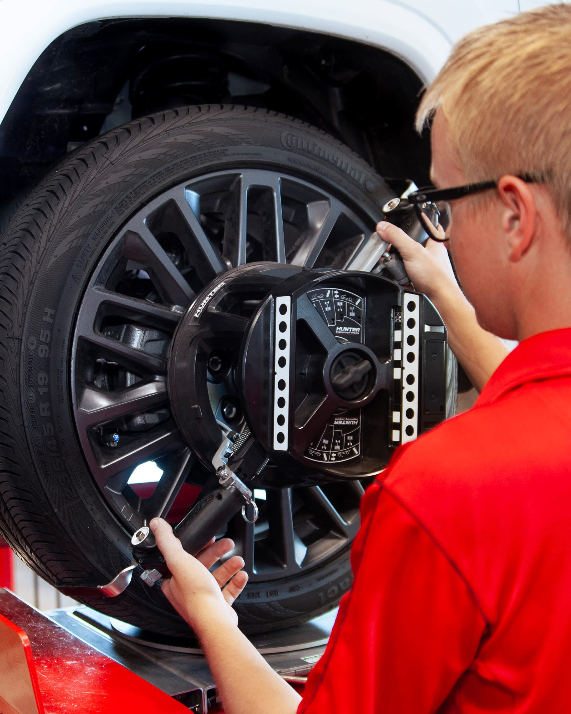 Discount Tire Fleet Services Auto technician in an orange shirt balancing a car wheel with professional alignment equipment — precision tire balancing and wheel alignment service for safer, smoother rides.