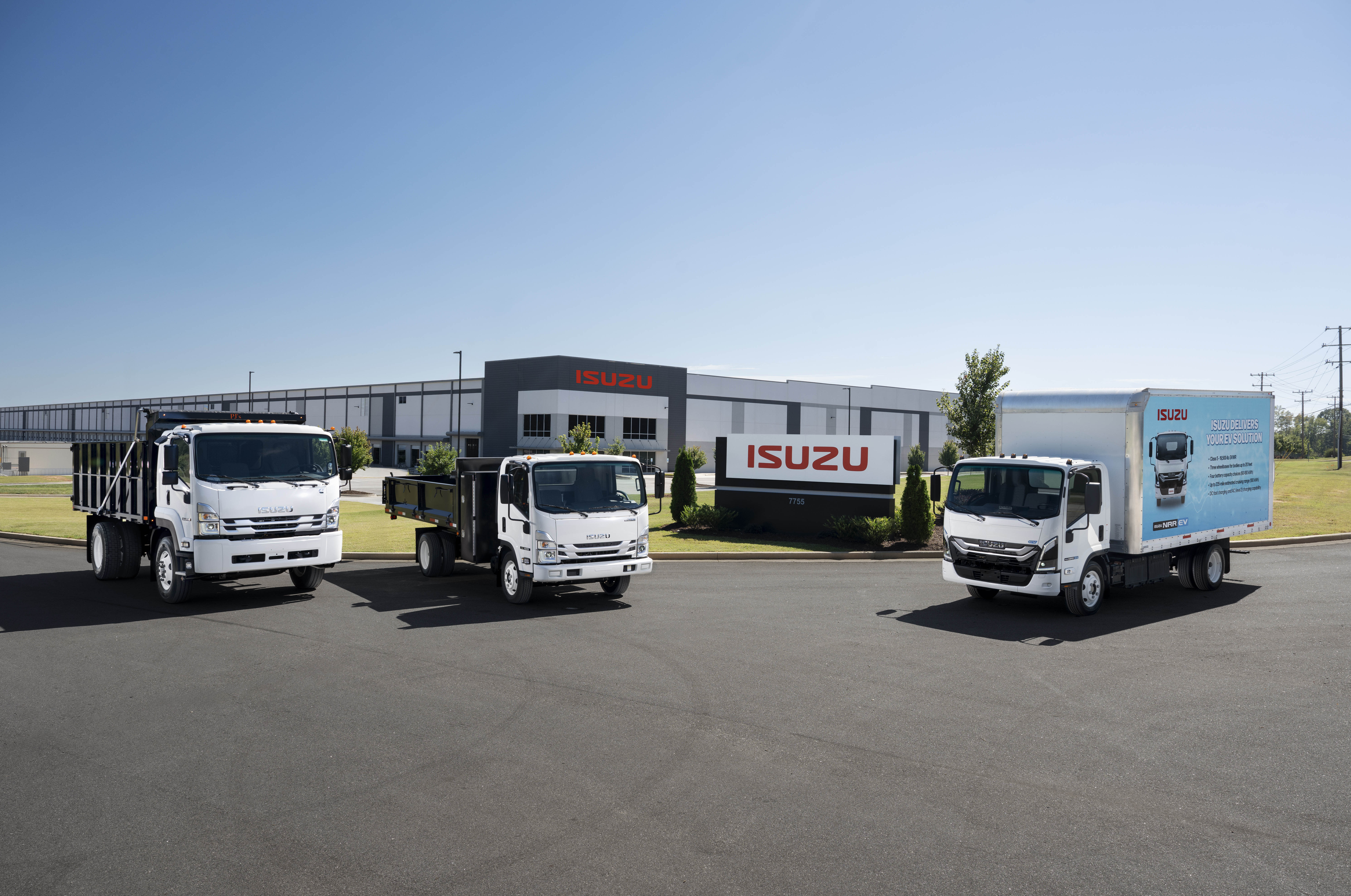 Isuzu commercial truck lineup parked outside a modern Isuzu warehouse: light-duty cabovers and box truck showcased for fleet buyers and rentals.