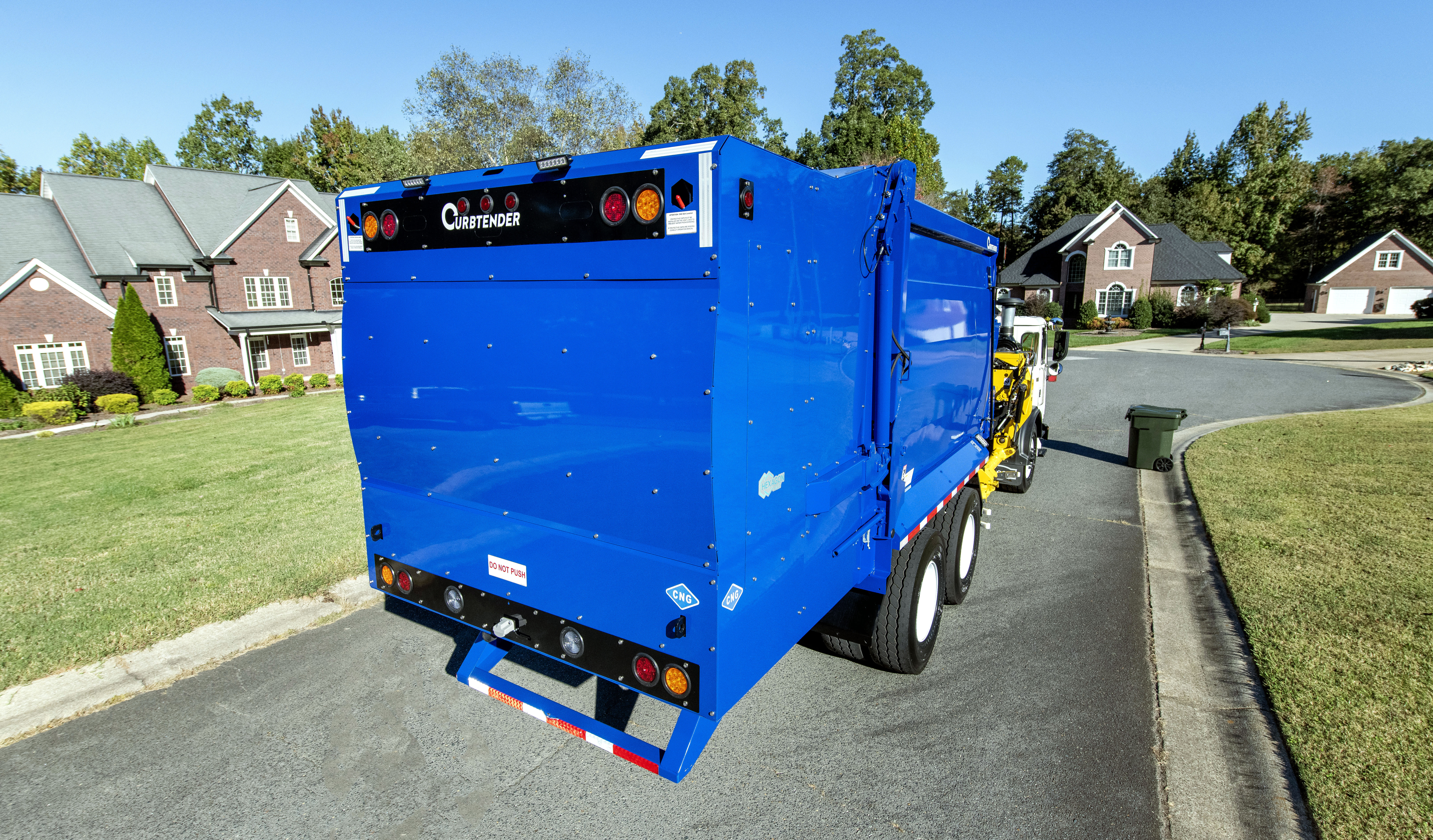 Hexagon Agility CNG Tailgate fuel system for refuse. Image contains a bright blue curbside garbage truck with Curbtender logo in black and white panel of rear tail gate. The trailer is parked on a sunlit suburban street, ready for pickup amid manicured lawns and brick houses in a peaceful neighborhood.