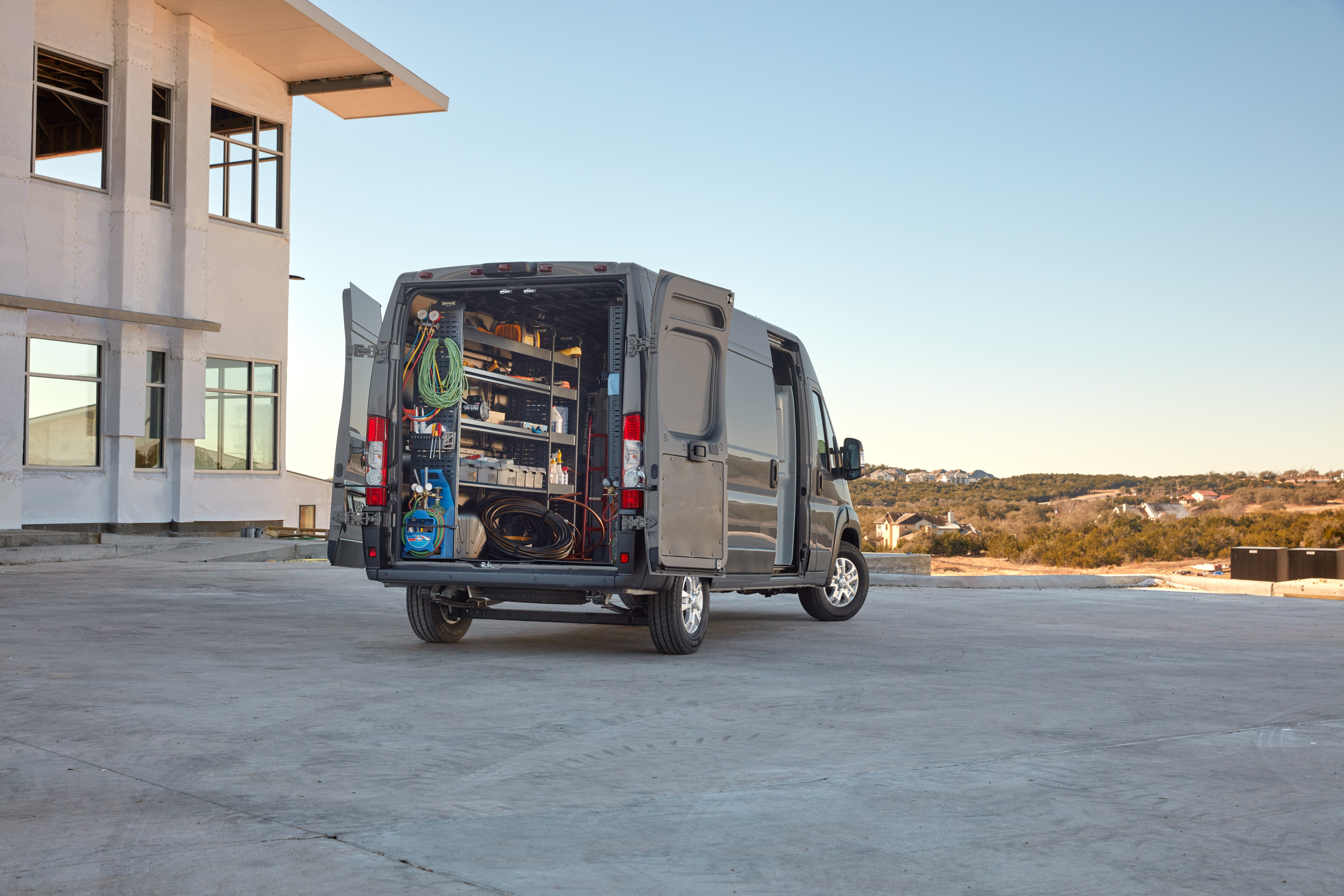 Black commercial cargo van with rear doors open, showing organized tools and equipment at a job site.