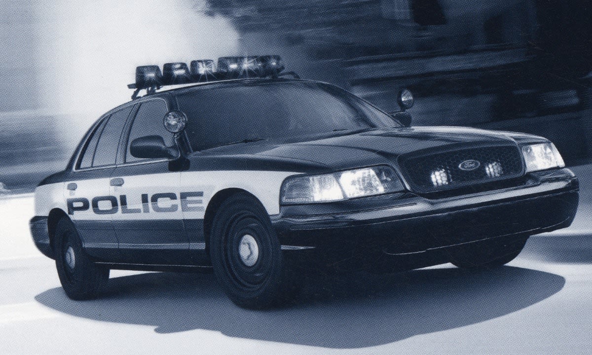 Black and white police patrol car in motion with emergency lights