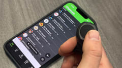 Closeup photo of man's hand using a thumg to push a push to talk button with phone on table.