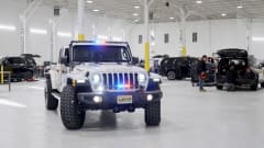 Police Jeep with light activated inside a garage with other vehicles being worked on in the background.