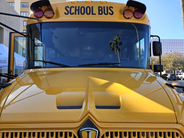 a close up of the front of a school bus with a palm tree reflection in the windshield