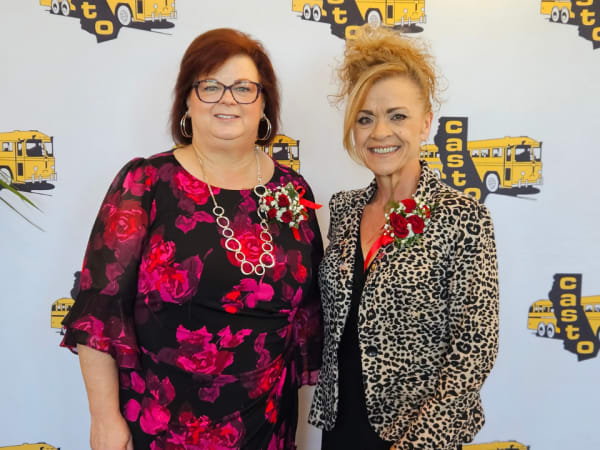 Two conference leaders pose for a portrait in front of a CASTO step-and-repeat backdrop featuring school bus logos.
