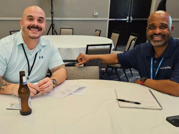 Two attendees smile while seated at a networking table during a meet-and-greet event sponsored by EverDriven.