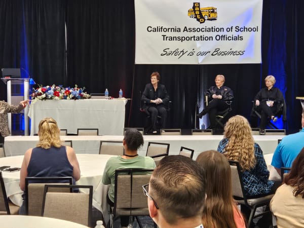 Panelists sit on stage during a moderated discussion session while attendees listen from round tables in the conference ballroom.