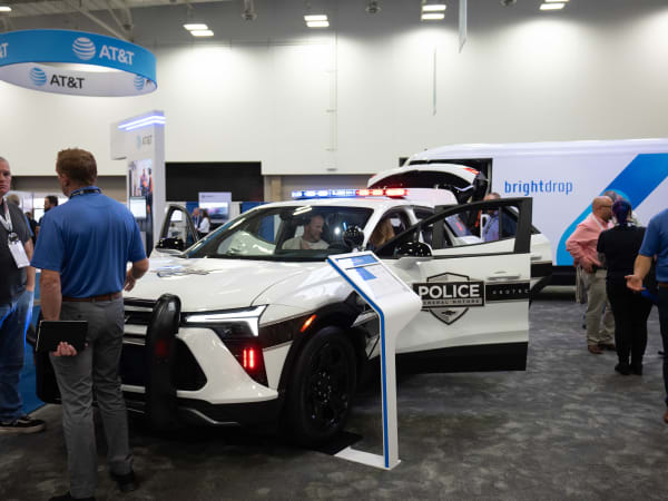 A white Chevrolet Blazer EV PPV is shown with its lights flashing and attendees gathered around it in an Exhibit Hall.
