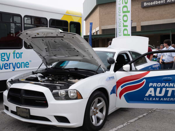 A white Dodge Charger Pursuit is shown with its hood up and door open. The vehicle has a propane autogas decal on the side.