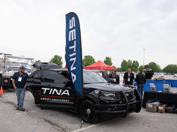 A black Ford Police Interceptor Utility with a Setina Manufacturing decal is shown with doors open and people gathered around. 