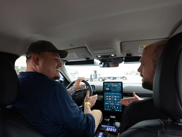 An attendee sits in the driver's seat of a Ford Mustang Mach-E, chatting with a person in the passenger's seat.