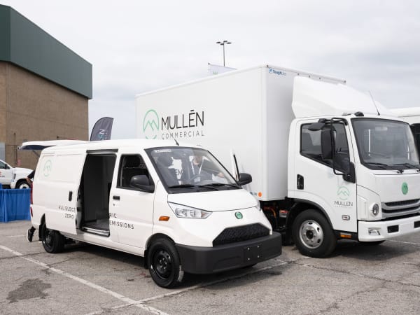 A Mullen One cargo van sits next to a Mullen Three low cab forward truck on display.