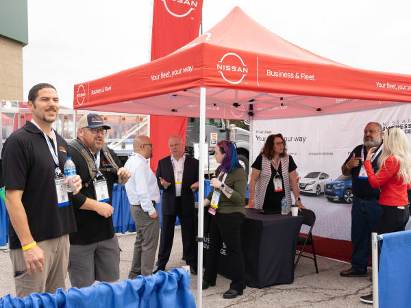A group of people chatting under a Nissan tent is shown.
