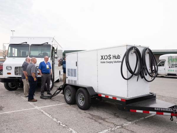 An XOS Hub mobile charging solution sits in the parking lot, with attendees looking at it.