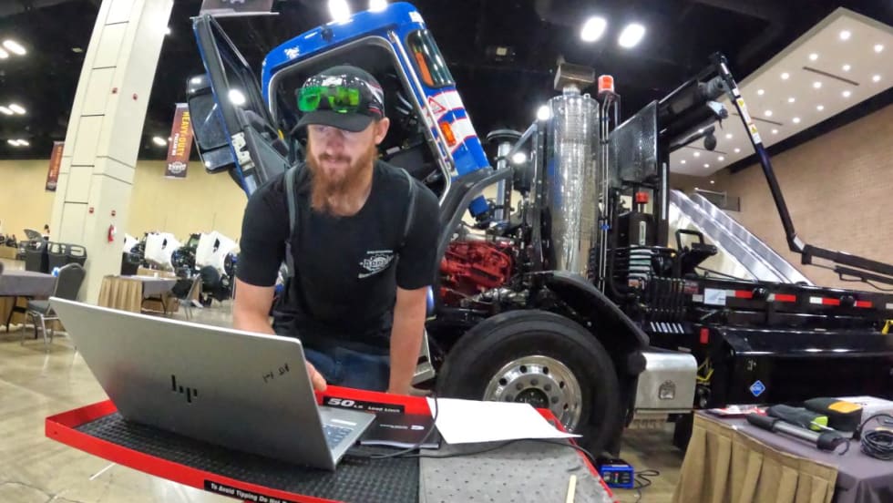 Male technician bent over a laptop computer in front of a line of CNG trucks in a maintenance shop.