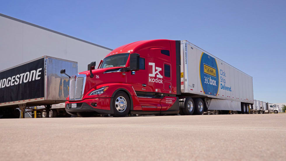 Red Kodiak Robotics truck tractor pulling J.B. Hunt 360 trailer with Bridgestone trailer in background.