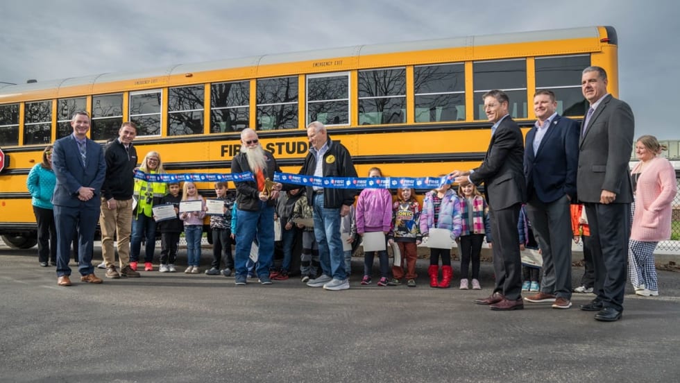 two people in safety vests walk in front of school buses