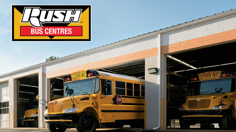 Two yellow school buses are parked in service bays at a dealership under the Rush Bus Centres logo.