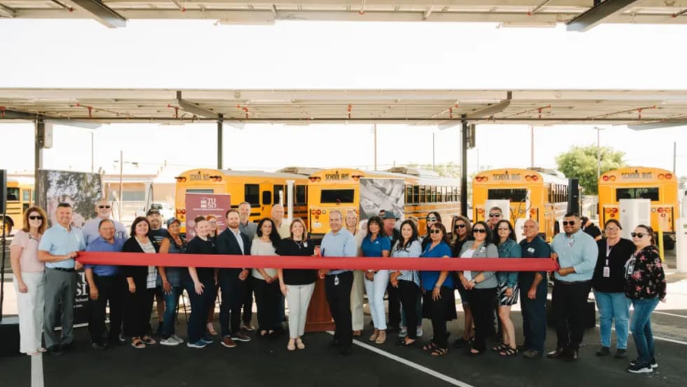 Turlock Unified staff and partners hold a ribbon-cutting in front of new electric school buses under solar canopies at the district transportation center.