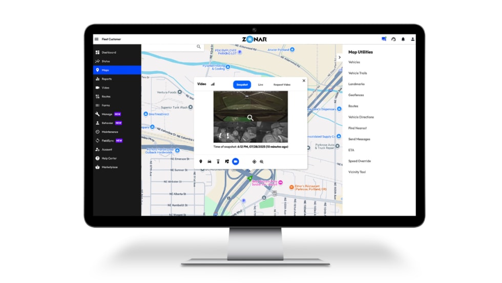 Computer monitor displaying Zonar Ignition’s fleet management interface, showing a city map with vehicle locations and an inset video snapshot from inside a vehicle’s cabin.