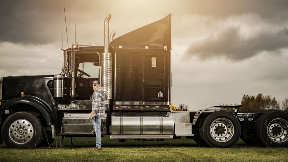 Moody photo of a black classic style commercial truck with a driver standing beside it.