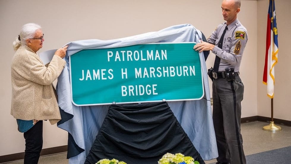Police officer and elderly woman unveiling Patrolman James H Marshburn Bridge sign