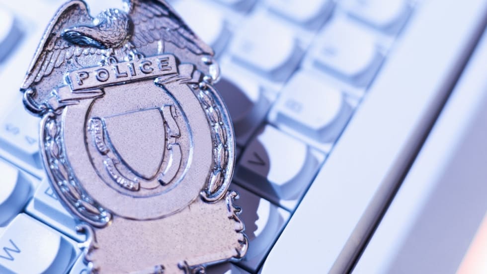 Silver police badge with eagle emblem resting on computer keyboard