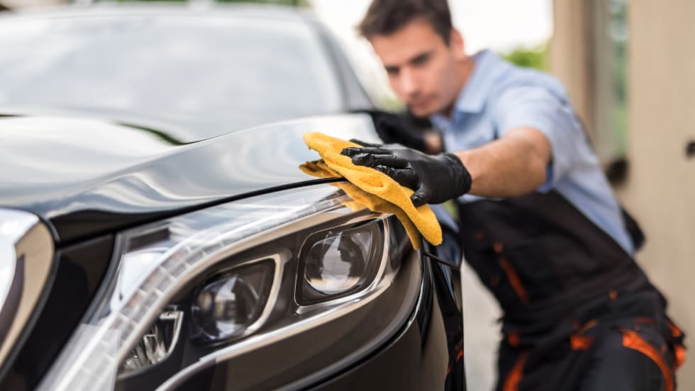 Technician polishing a car headlight with a microfiber cloth, representing Protective Asset Protection’s enhanced Appearance Protection program for long-term vehicle surface care.