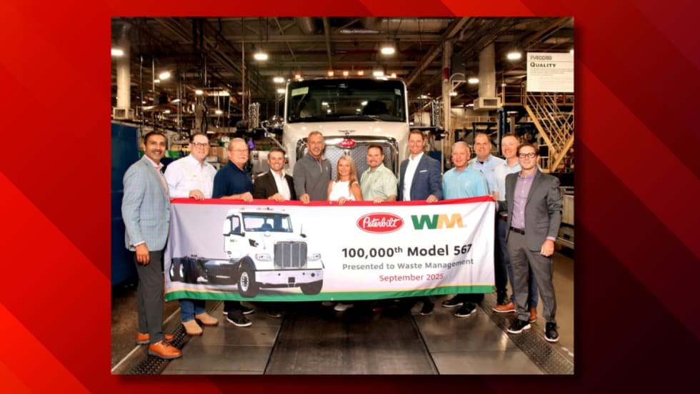 Peterbilt and WM representatives stand in front of the 100,000th Model 567 truck during a ceremony at Peterbilt’s Denton, Texas, manufacturing facility, holding a banner marking the milestone.
