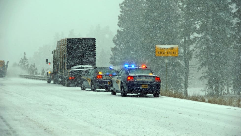 Police vehicles escorting truck on snowy highway during winter storm
