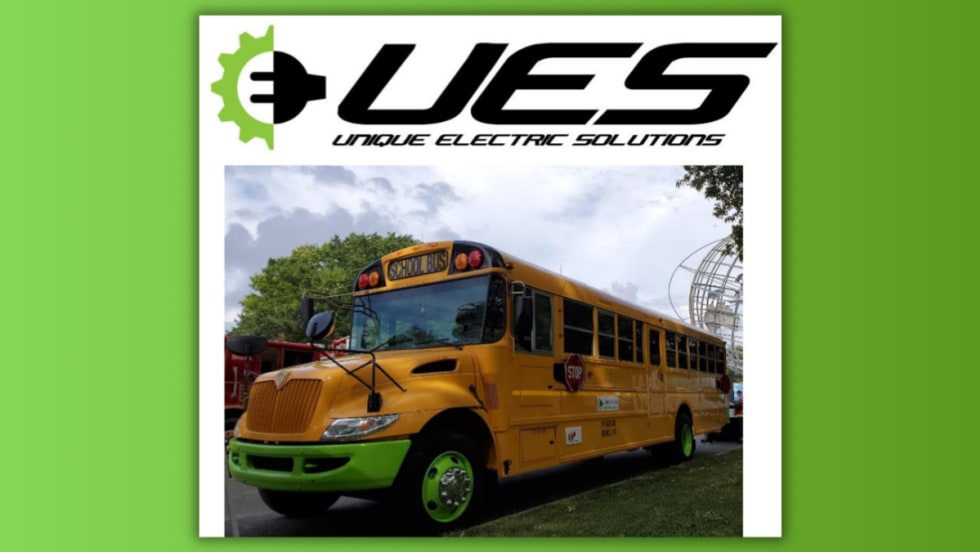 A repowered electric school bus with green wheels and accents, designed by Unique Electric Solutions, parked outdoors under cloudy skies with the company’s logo displayed above the image.