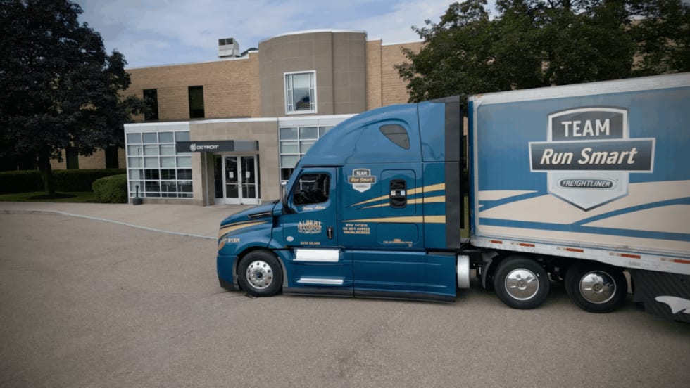 A blue Freightliner Cascadia truck operated by Albert Transport and branded with the Team Run Smart logo parked outside a Detroit Diesel facility.
