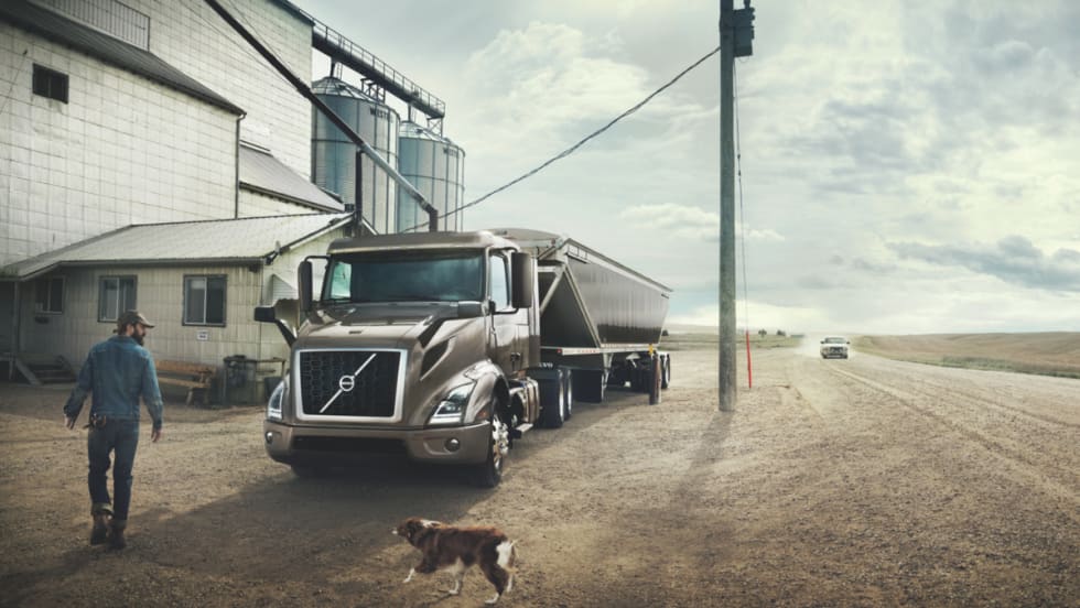 Volvo truck parked at a rural location with a driver and dog nearby.