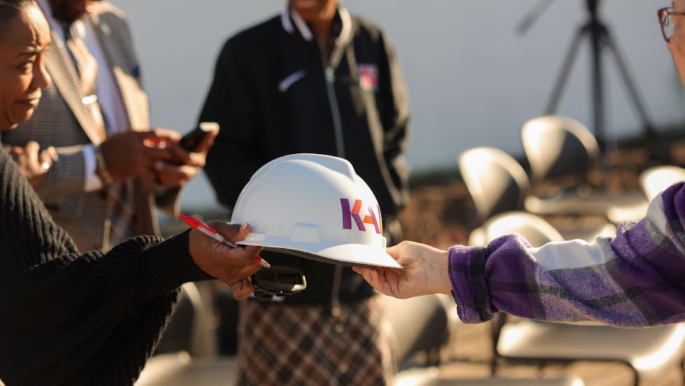 Close-up of a construction hard hat being handed to an attendee at the Normandy Schools Collaborative groundbreaking event.