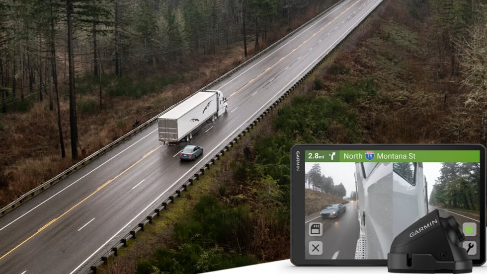 An overhead view of a tractor-trailer traveling on a two-lane highway, with an inset showing a Garmin in-cab display and side-mounted camera view of a passing vehicle.