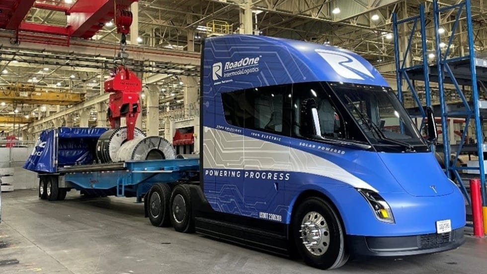 Blue Tesla Semi pulling flatbed trailer inside warehouse or manufacturing facility