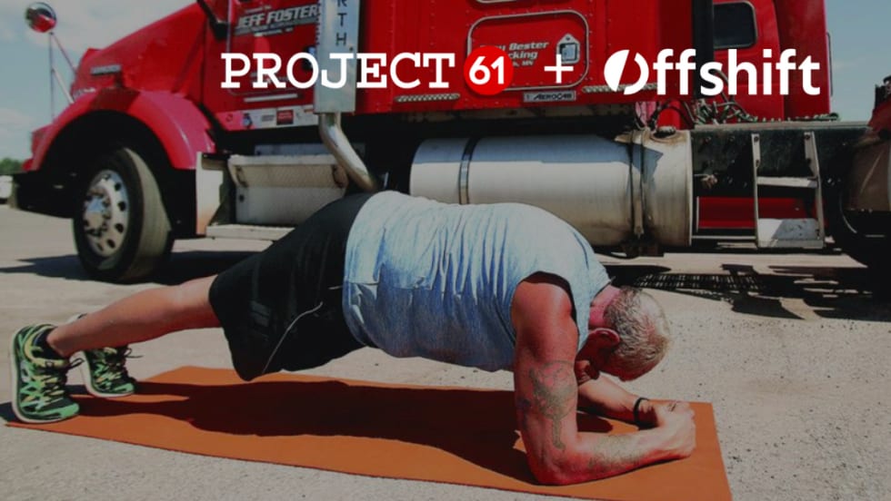 Truck driver doing a plank exercise on a mat with a red truck in the background.
