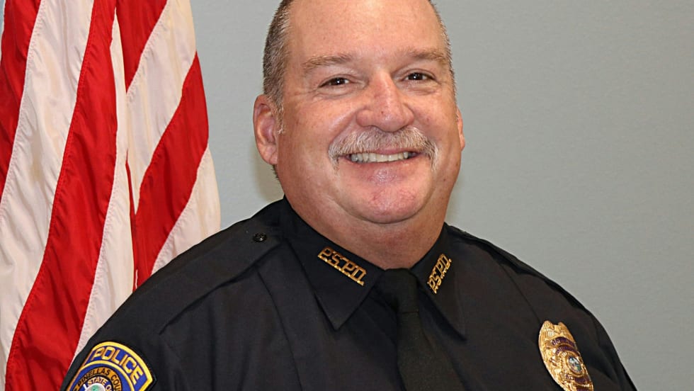Smiling police officer in black uniform standing in front of American flag