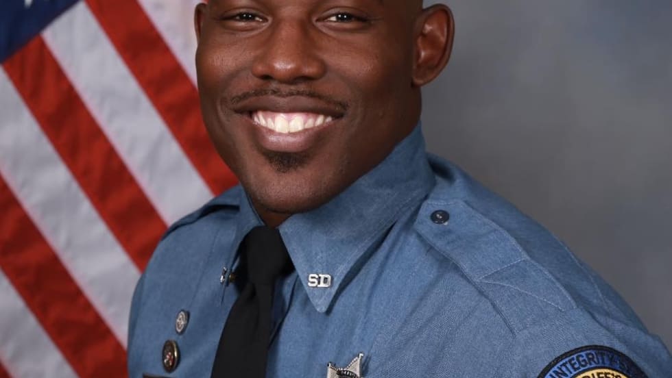 Smiling sheriff's deputy in blue uniform with American flag background