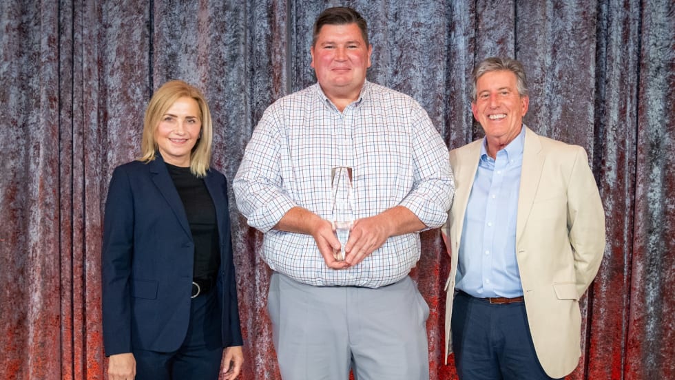 A photo of three people holding a trophy on a stage