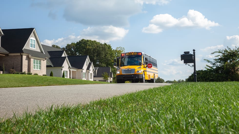 a photo of a school bus driving down a suburban street with houses in the background and green grass pictured