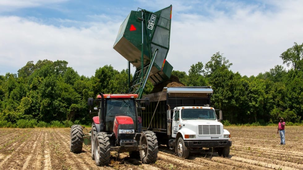 Tractor loading a farm truck in a field.